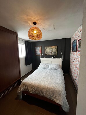 A bedroom with a bed, a hanging light fixture, a white dresser, and two framed pictures on the wall.