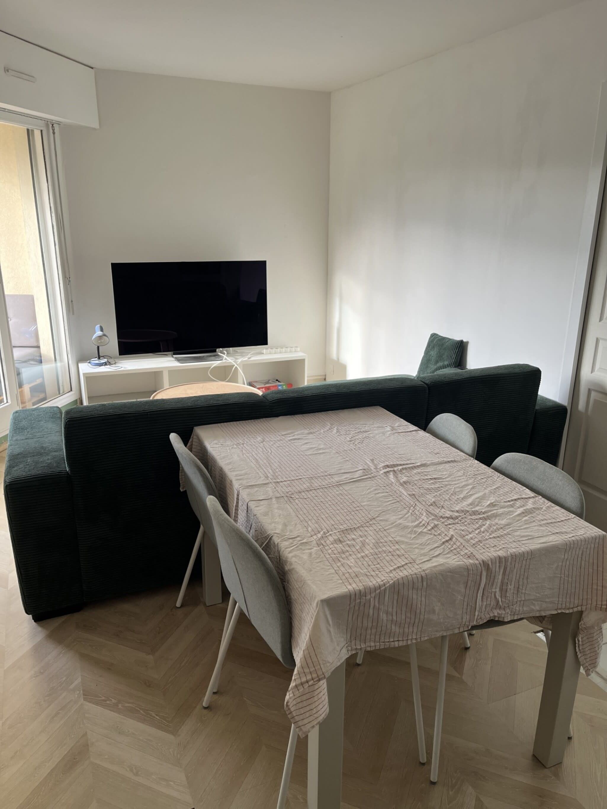 A modern living room with a flat-screen TV, a sofa, a dining table, and a chair.