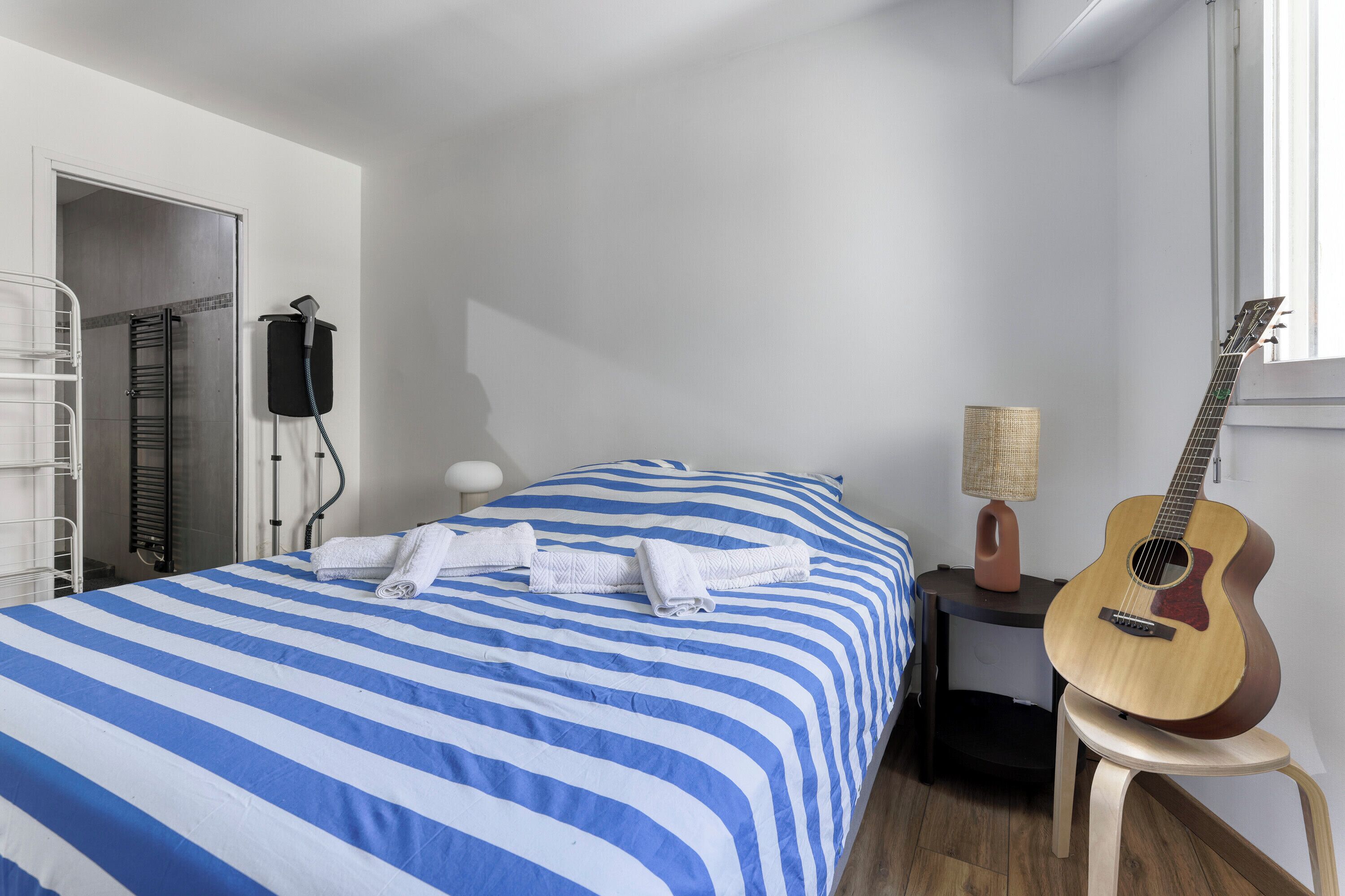 A room with a bed, a guitar, a lamp, and a towel rack.