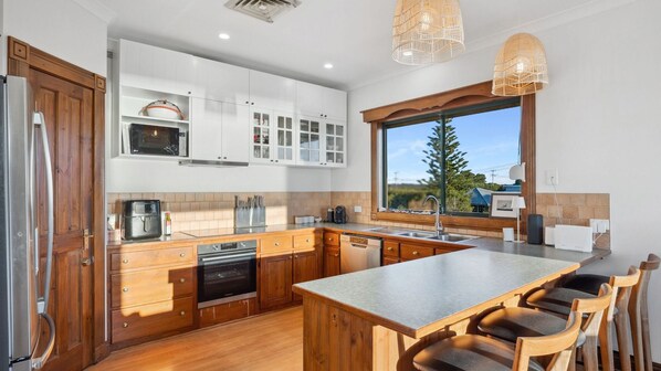 A modern kitchen with wooden cabinets, a large island, and a view of the outdoors. - Peppy View Beach House (Peppermint Grove Beach)