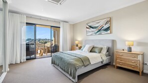 A spacious bedroom with a large bed, two bedside tables with lamps, a view through a sliding glass door, and a painting on the wall.