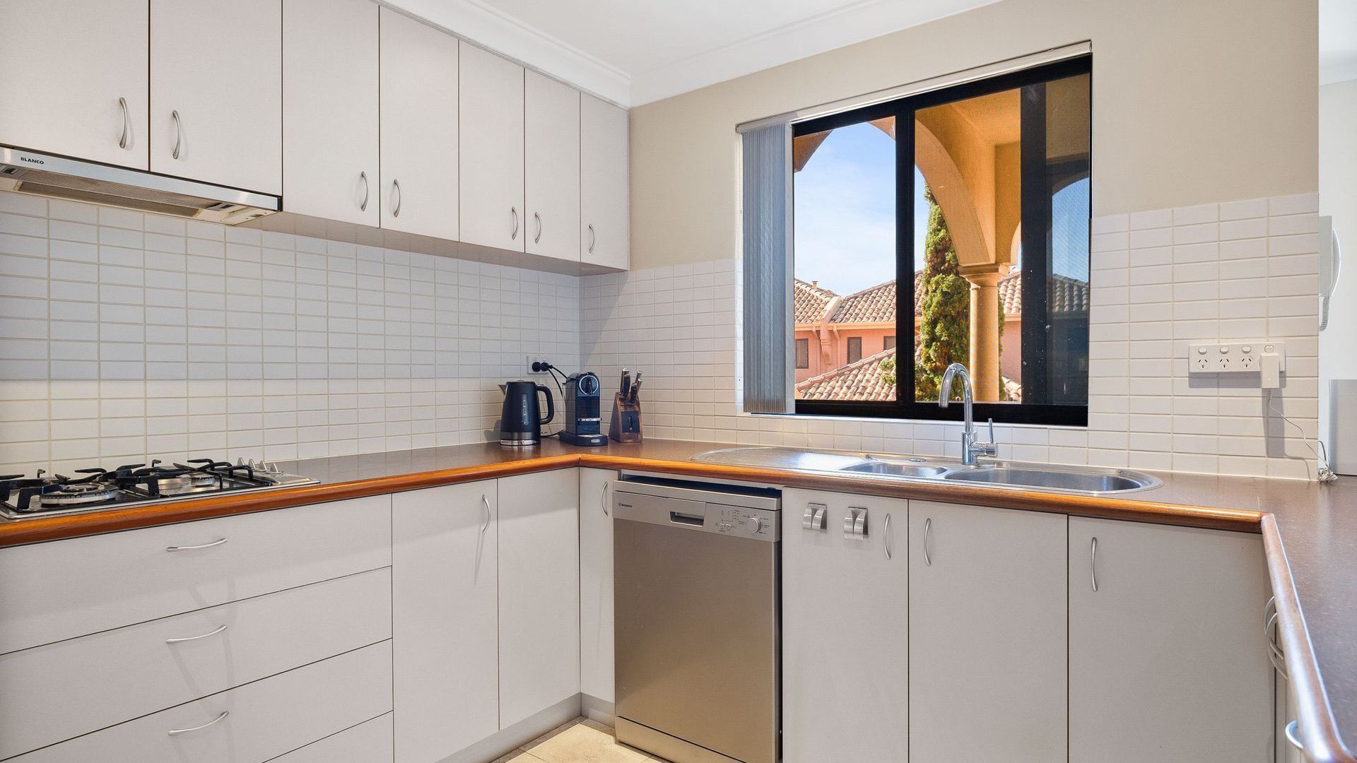 Cocina moderna con gabinetes blancos, lavavajillas, estufa y ventana con vistas a edificios.