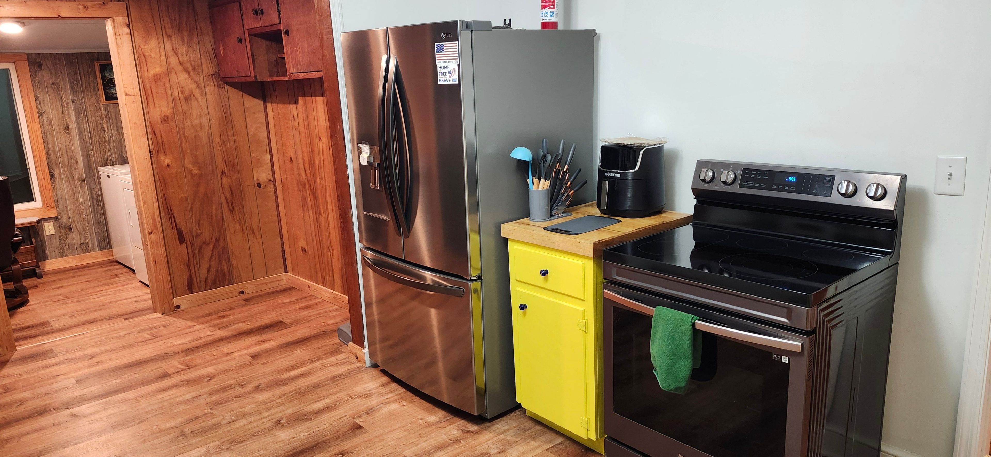 A compact kitchen with a stainless steel refrigerator, a yellow cabinet, and a black oven.