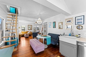 A spacious living area with a wooden staircase, a dining table, a sofa, and a kitchen with a sink.