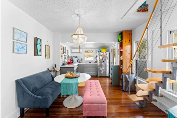 A modern kitchen with a dining area, a staircase, and a living room with a sofa and ottoman.