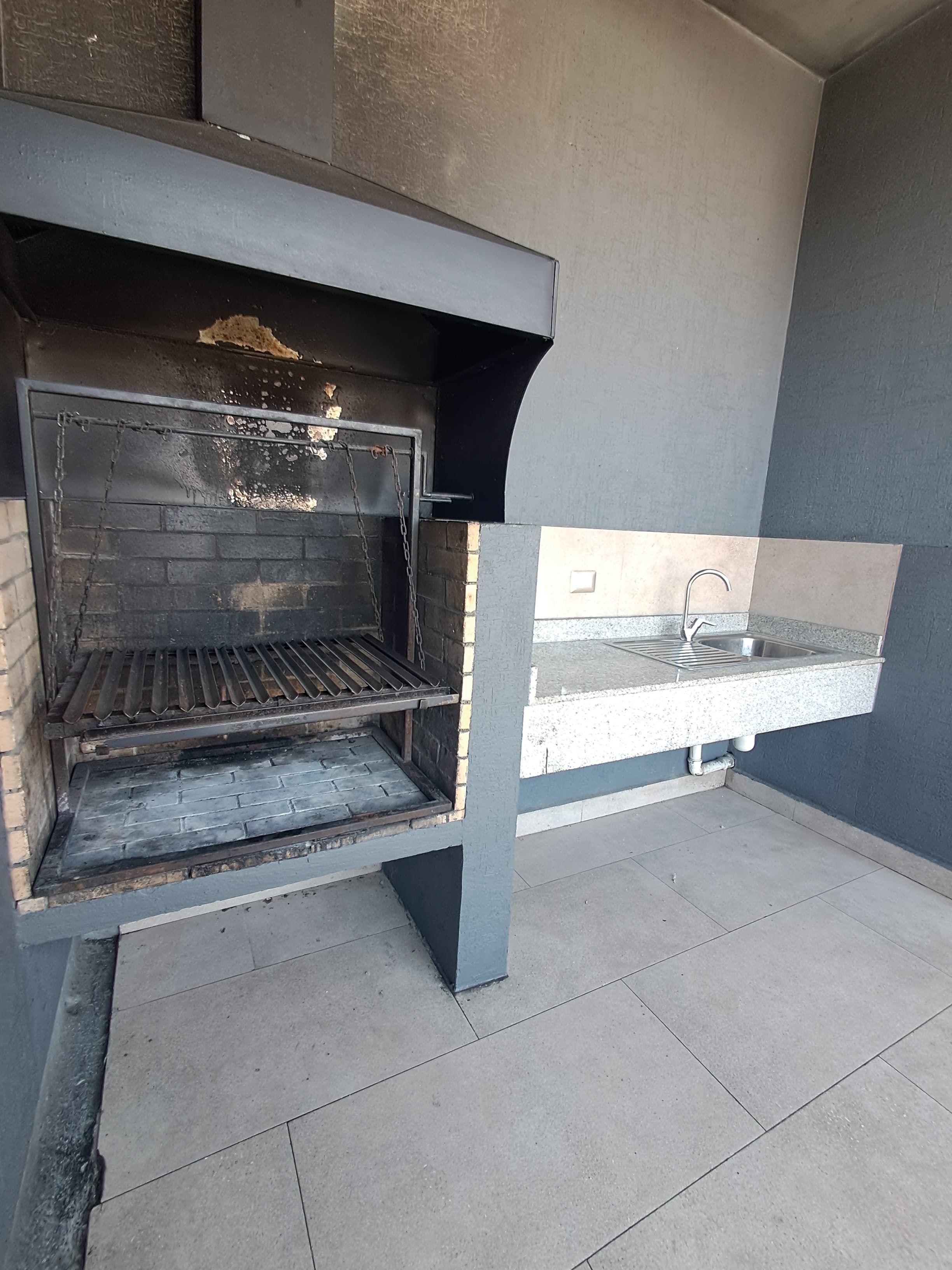 Una parrilla exterior con interior de ladrillo, rejilla metálica y pileta de acero inoxidable.