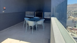 En tagterrasse med grill, siddepladser og udsigt over byen.