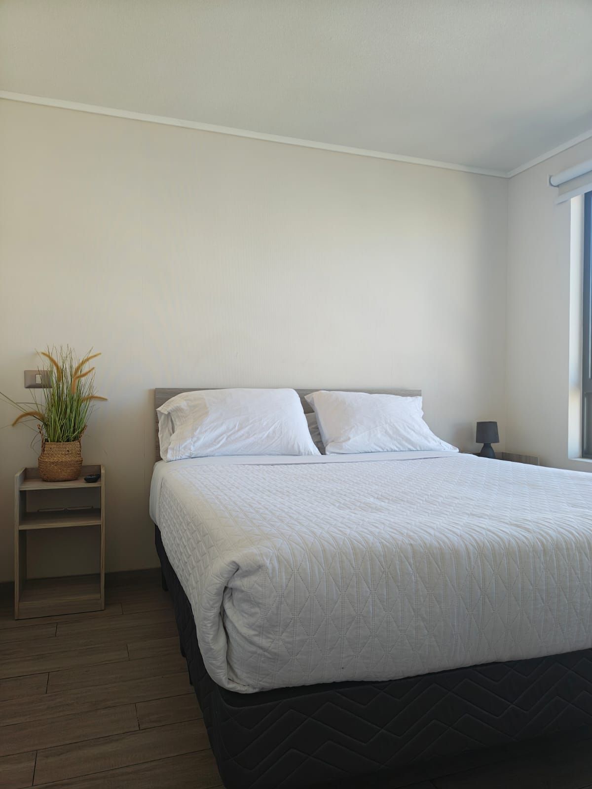 Un dormitorio con cama, mesita de noche, lámpara y ventana.