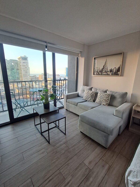 A modern living room with a large window, a sofa, a coffee table, and a city view.