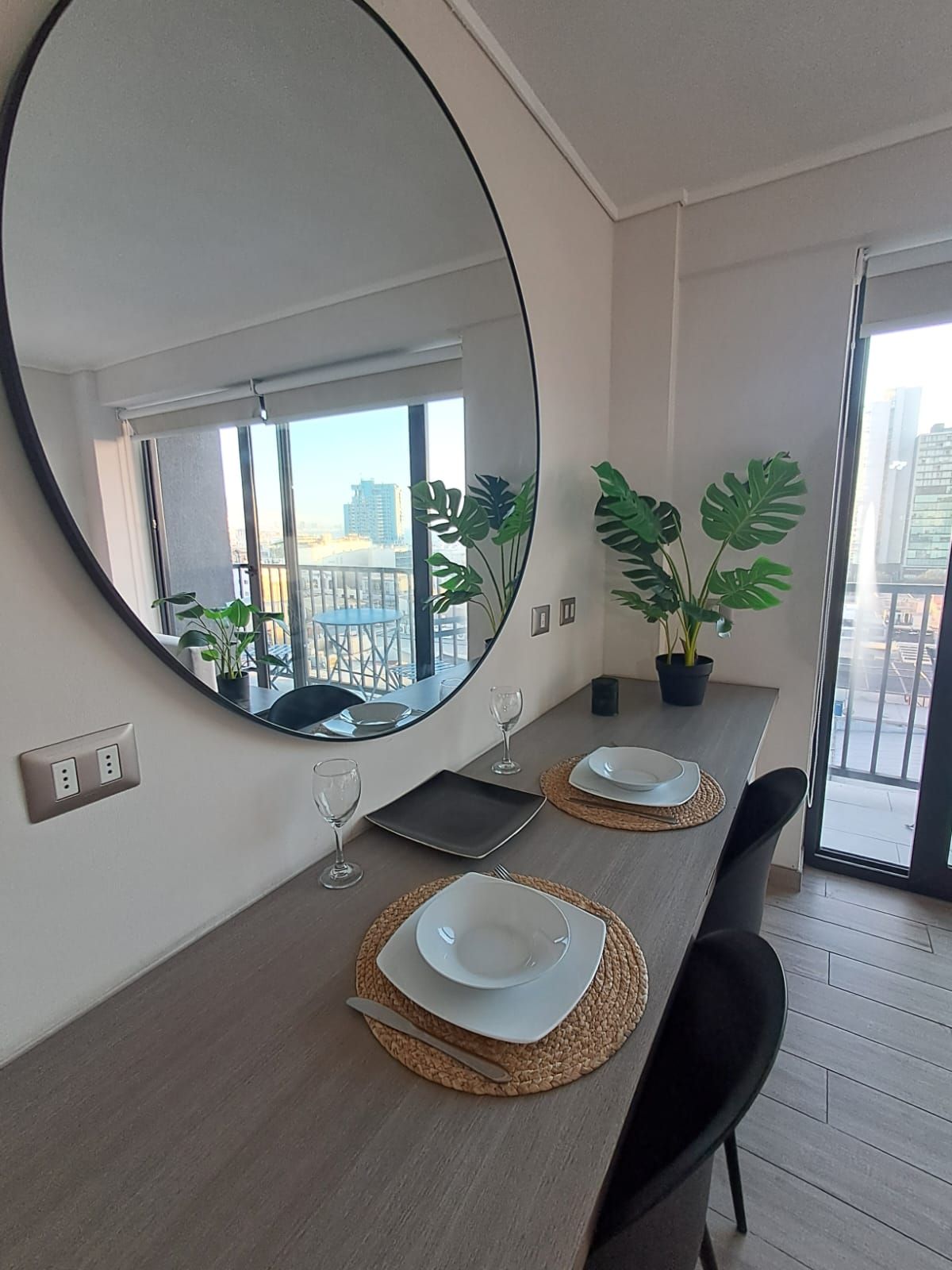 Un comedor moderno con un espejo grande, dos plantas en macetas y una mesa para dos comensales.
