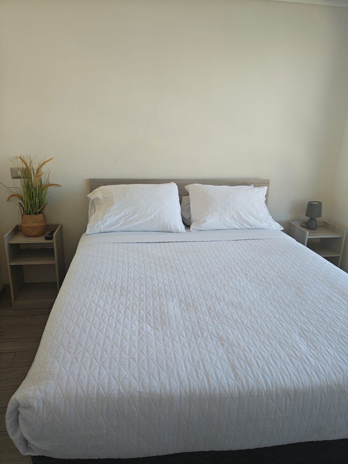 A neatly made bed with a quilted white duvet, two pillows, and a wooden headboard.