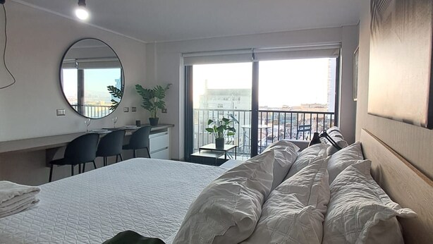 Et hotelværelse med seng, skrivebord, stol, stort vindue og balkon.