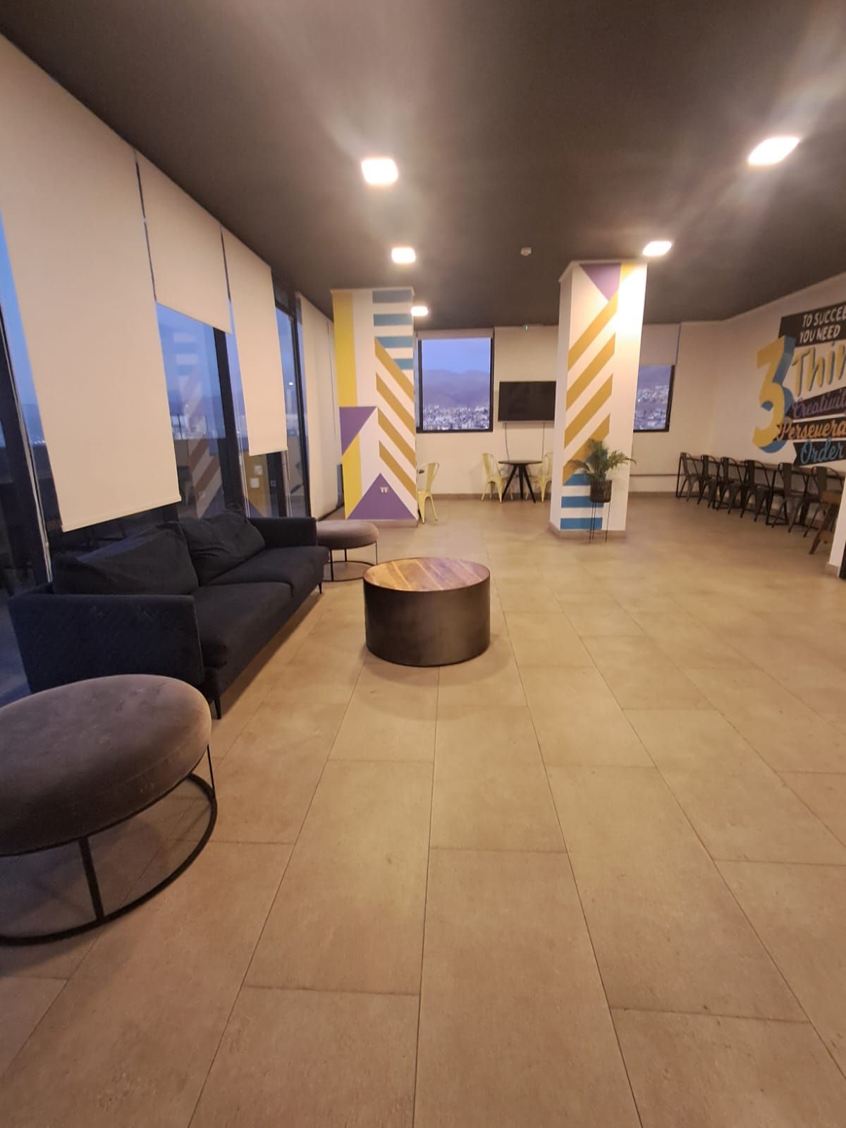 Ampla área de estar com um sofá, uma mesa de centro redonda e um espaço com cadeiras.
