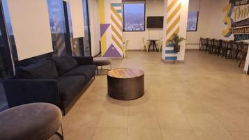 Ampla área de estar com um sofá, uma mesa de centro redonda e um espaço com cadeiras.