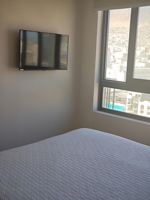 Una habitación con una cama, un televisor de pantalla plana en la pared y un ventanal con vistas a edificios.