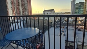 En balkon med et rundt bord og blå stole, der udover en by udsigt med bygninger og en klar himmel.