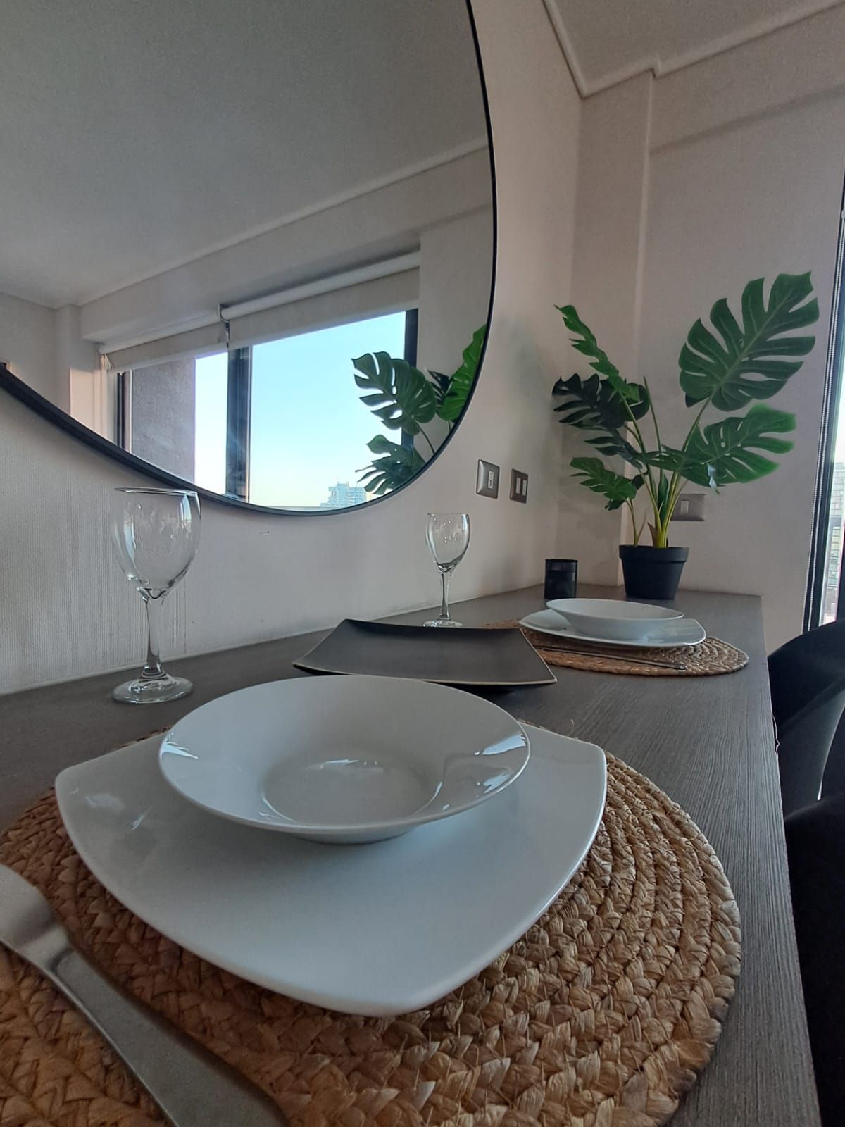 Uma área de refeições com uma mesa posta para dois, incluindo pratos, talheres e copos de vinho.