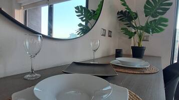 Uma área de refeições com uma mesa posta para dois, incluindo pratos, talheres e copos de vinho.