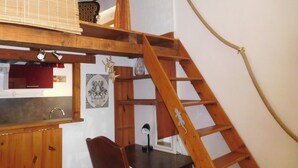 Parviolotyylinen makuuhuone, jossa on puinen tikapuu, joka johtaa ylätasanteelle, jossa on sänky. Tikapuiden alla on työpöytä ja tuoli, ja sen yläpuolella on ikkuna.