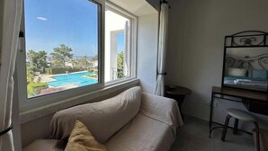 Habitación con un ventanal grande que ofrece vista a una piscina y follaje. Se observa una cama con cabecera y una pequeña mesa con una silla.