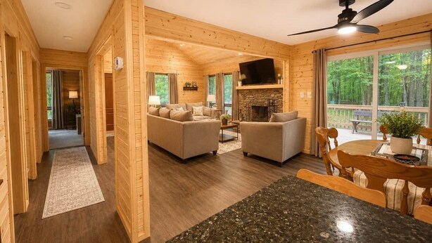A wooden cabin interior with a living room, dining area, and a fireplace.