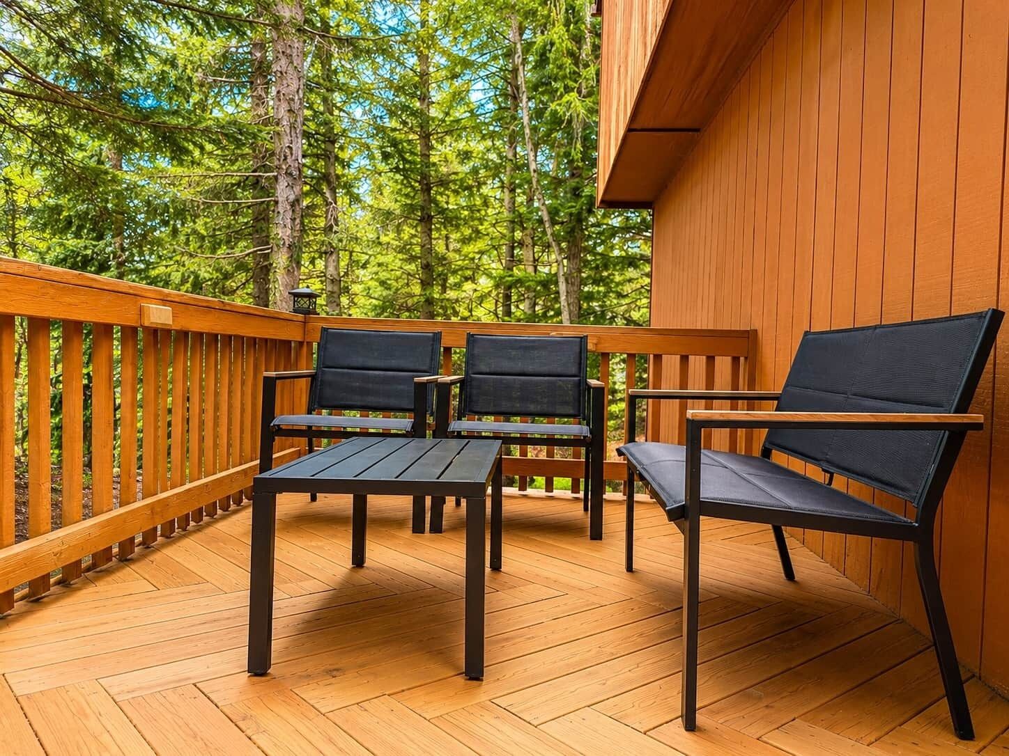 A wooden deck with four chairs and a table, surrounded by trees.