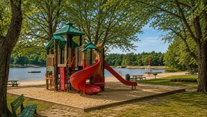 A playground with a slide and climbing structures near a lake.