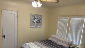 A bedroom with a bed, a ceiling fan, a door, and a window with blinds.