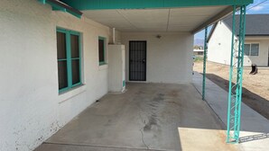 A covered outdoor area with a concrete floor, a white building with green trim, and a black door.