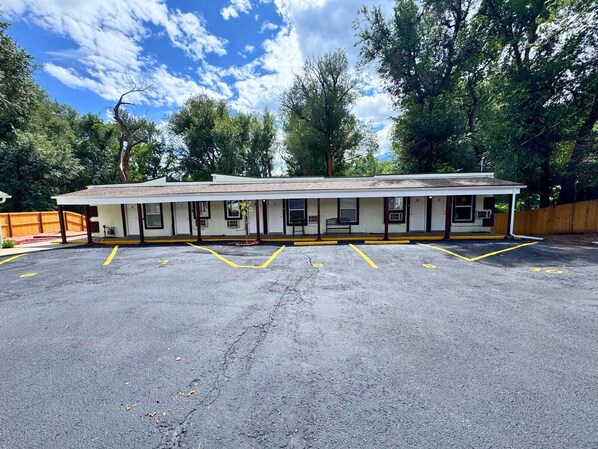 Un motel con una fila di camere, un'area di parcheggio coperta e alberi sullo sfondo.