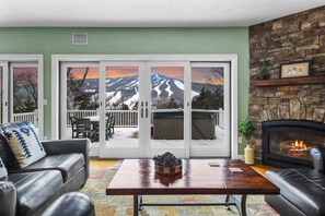 A living room with a fireplace, a sofa, a coffee table, and a sliding glass door leading to a deck with a view of mountains.