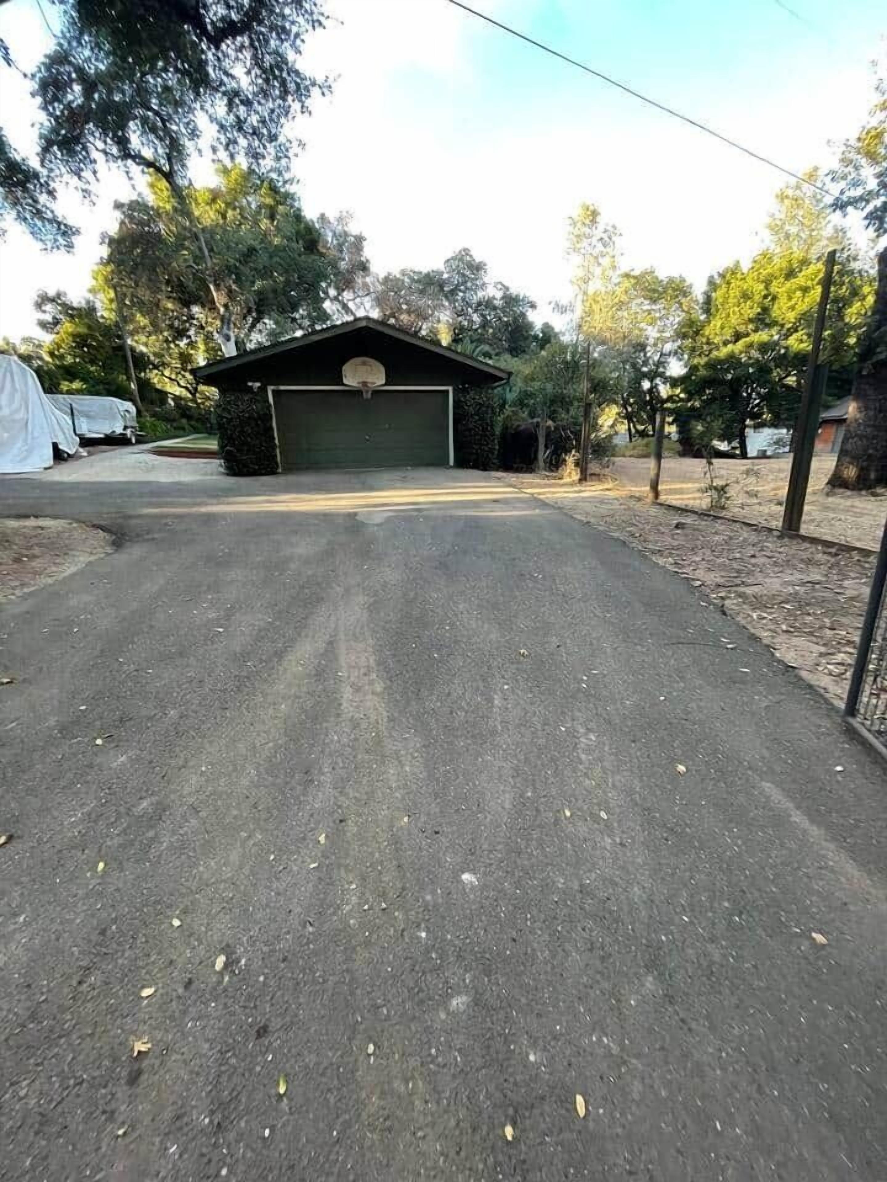 A garage with a covered driveway, surrounded by trees and a fenced area.
