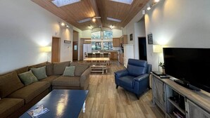 Un salón amplio con techo de madera, un televisor de pantalla plana grande, un sillón azul y un sofá.