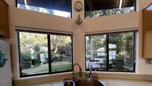 Una cocina con un lavamanos doble, armarios de madera y ventanas amplias que dan a un patio trasero.