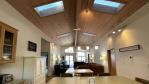 Una cocina amplia con una isla central, techo de madera, tragaluces y un comedor con sillas.