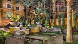 A courtyard with outdoor seating, palm trees, and a building in the background. - Sports fans, Luxurious 2-bed 2 Bath resort with pool, full kitchen washer/dryer (Las Vegas)