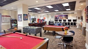 A pool area with multiple pool tables, a foosball table, and a billiards table. There are chairs and a small table with a vase of flowers. - Sports fans, Luxurious 2-bed 2 Bath resort with pool, full kitchen washer/dryer (Las Vegas)