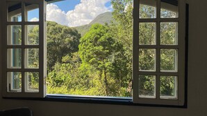 A room with a large window revealing a lush, green landscape with trees and a mountain in the distance.