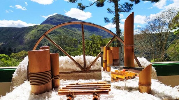 A rustic wooden water wheel setup with logs and wooden structures, set against a mountainous backdrop.