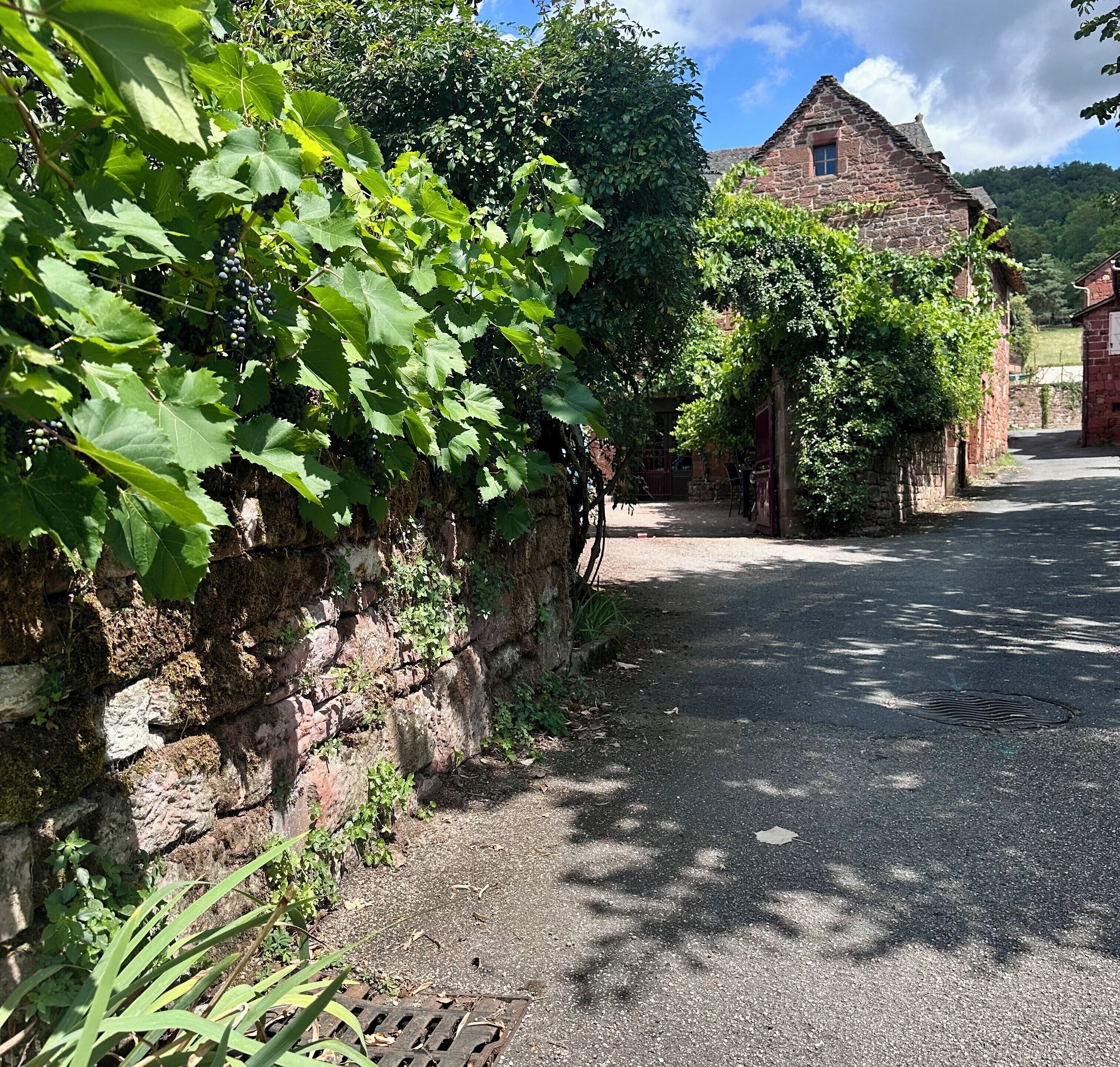A rural road with a stone wall and a building with a tiled roof.
