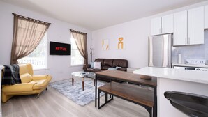 Un salon moderne avec un canapé jaune, une table basse en bois, un banc et un téléviseur fixé au mur.