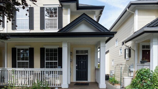 Une maison à deux étages avec un porche à l’avant, une porte noire et un petit jardin.