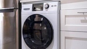 Une cuisine moderne dotée d’un réfrigérateur en acier inoxydable, d’un lave-linge à chargement frontal et de meubles de cuisine blancs.