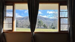 A room with a large window, curtains, and a view of a mountainous landscape.