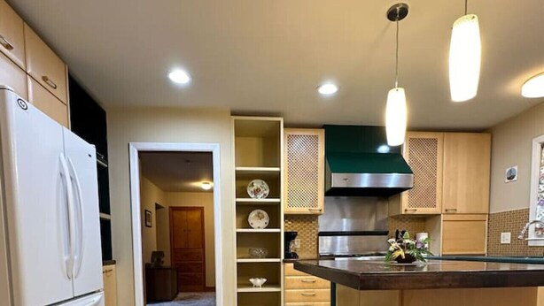 A modern kitchen with a central island, bar stools, and a refrigerator.