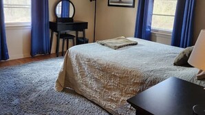 A bedroom with a bed, a desk, a chair, a lamp, and a picture on the wall.