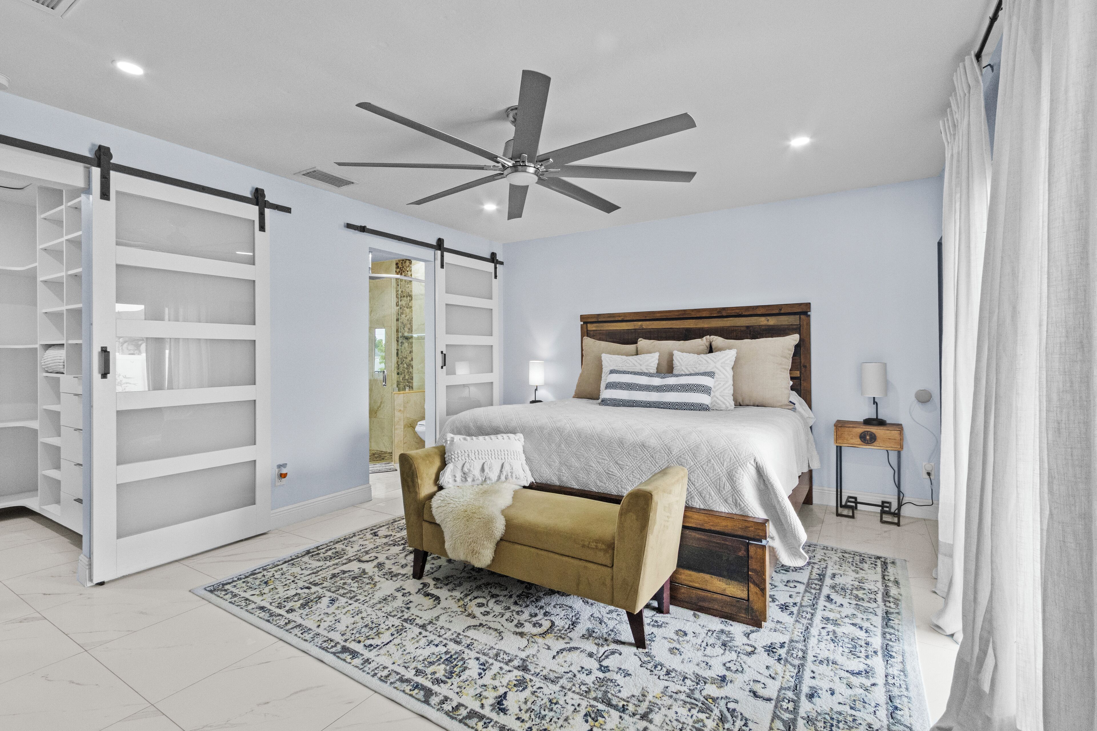 Une chambre à coucher comprenant un lit, un ventilateur de plafond, une table de chevet, une commode, une armoire et un tapis à motifs.
