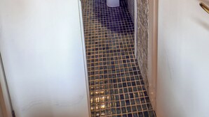 Een smalle gang die leidt naar een badkamer met een wastafel, spiegel en betegelde vloer.