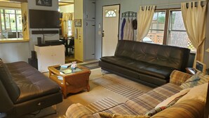 A living room with a black leather sofa, a wooden coffee table, and a striped rug. There is a television on the wall and a door leading to another room.
