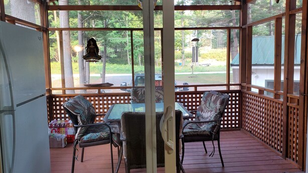 A covered outdoor area with a table and chairs, a refrigerator, and a view of the surrounding greenery.
